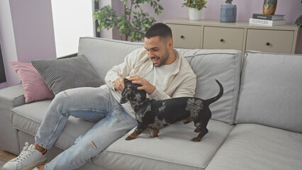 Hispanic man enjoying time with his dachshund dog in the cozy living room of an apartment.