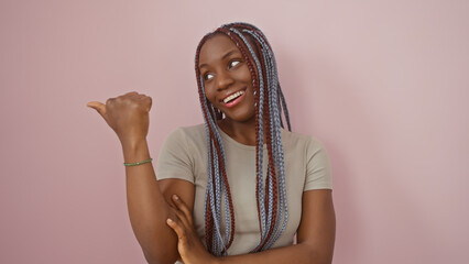 African american woman with braids smiling and pointing thumbs up against a pink isolated background