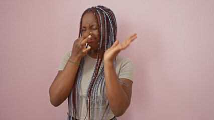 African american woman with braids expressing disgust against a pink background.