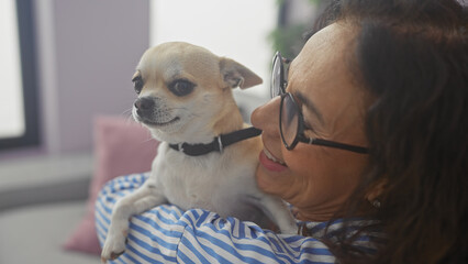 A middle-aged woman cuddles her chihuahua indoors, conveying warmth and companionship in a cozy...