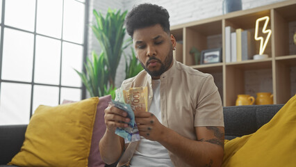 Handsome man counting canadian dollars indoors, portraying wealth or finances at home setting.