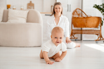 a baby learns to crawl on the floor, a small child crawls, a young mother and son, happy motherhood and maternity leave, mother and baby family, parents