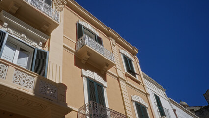 Elegant balconies and shutters adorn a charming two-story building against a clear blue sky in the old town of puglia, italy.