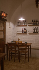 An intimate italian restaurant indoors with a cozy table setup, rustic brick walls, wooden chairs, shelves of wine bottles, and dim lighting creating a warm ambiance.