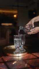 A person pours water from a bottle into glasses on a tray set upon a wooden surface.