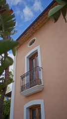 A vibrant peach-colored mediterranean building with a tiled roof, ornate balcony, and lush green foliage.