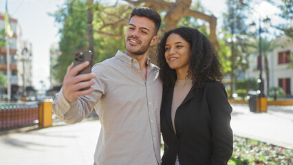 A man and woman enjoy a selfie together in a sunny city park, embodying love, togetherness, and outdoor leisure.