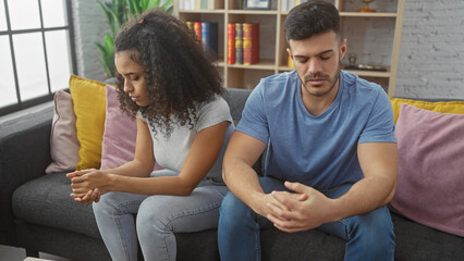A contemplative couple sits apart on a gray sofa in a serene living room, conveying a sense of a troubled relationship.
