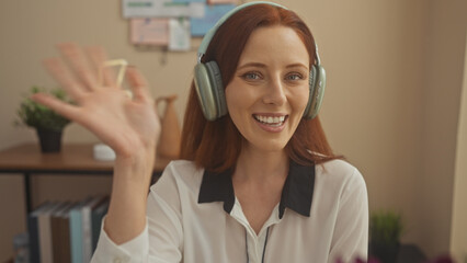 A smiling young woman with headphones enjoys a video call at her cozy home office.