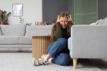 Young woman having panic attack near sofa at home