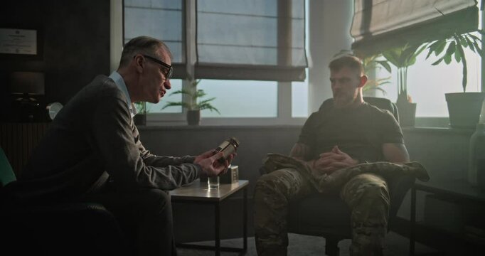 Senior psychiatrist talks to patient, gives antidepressants or sedative medicines to military man with PTSD. Psychotherapist conducts psychological therapy or post war rehabilitation for soldier.