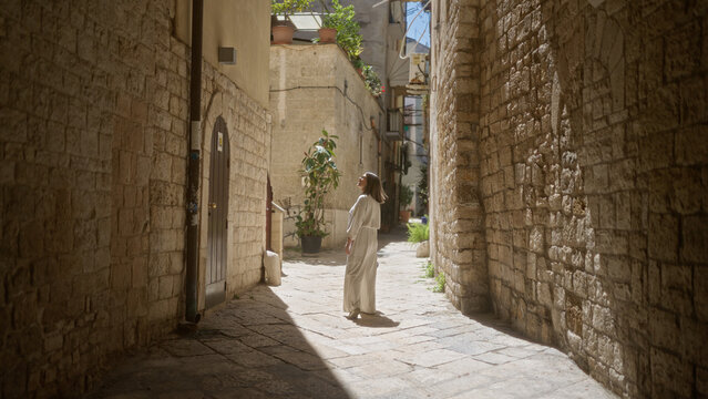 Fototapeta A young hispanic woman walks through the charming, sunlit old town streets of bari, puglia, italy.