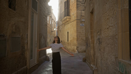 A young hispanic woman joyfully explores a picturesque alley in lecce, puglia, italy, surrounded by historic stone buildings bathed in warm sunlight.