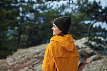 An adventurous woman in stylish orange raincoat and beanie conquers the summit of a majestic...