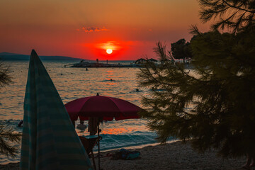 Sunset view over a ocean with a red umbrella and tree silhouette.
