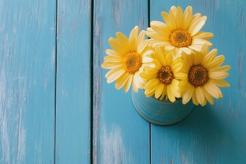 Yellow daisies in a vase on a blue wooden table, top view with copy space