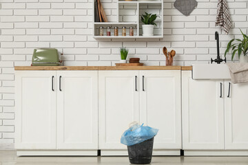 Full trash bin on floor in kitchen