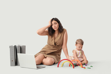Tired businesswoman and her little baby playing with toys on light background