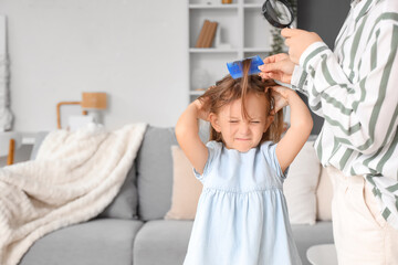 Mother with magnifier combing her little daughter's hair with pediculosis at home