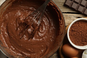 Chocolate dough in bowl among ingredients on wooden table, flat lay
