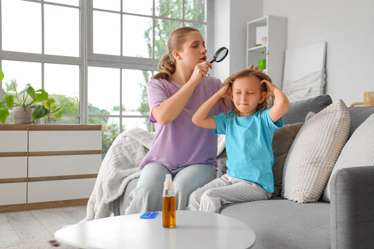 Mother with magnifier checking her little daughter's head with pediculosis at home