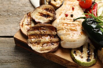 Delicious grilled vegetables and chicken breast on wooden table, closeup
