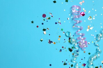 Shiny confetti and party streamers on light blue background, flat lay. Space for text