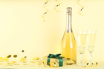 Shiny confetti, streamers, sparkling wine and gift box on beige background. Space for text