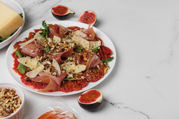 Close-up of a delicious appetizer of carpaccio made of figs, prosciutto, arugula and parmesan, sprinkled with walnuts on a plate. Copy space