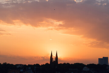 Fototapeta premium Morning sun rising among two church towers. Beautiful cozy sunrise over the city.