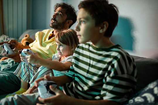 Father and children playing video games together on couch
