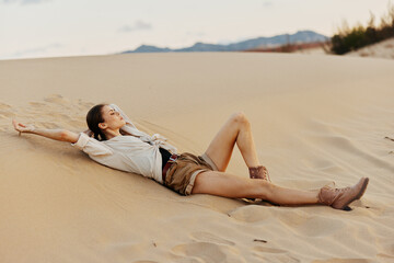 Lonely woman laying on top of a sand dune in the vast desert landscape under the scorching sun