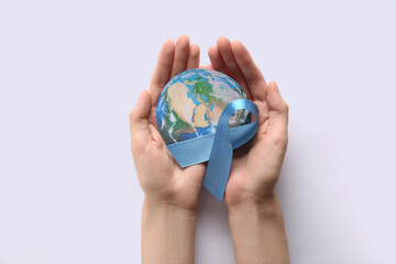 Female hands with blue ribbon and paper planet Earth on white background. World Cancer Day