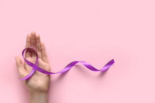 Female hand with purple ribbon on pink background. World Cancer Day