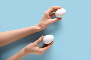 Female hands with raw chicken eggs on blue background