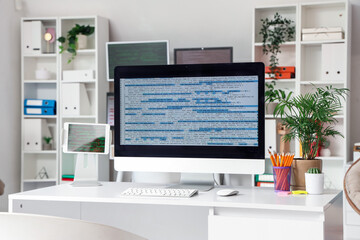 Fototapeta premium Computer monitor with code and plants on programmer's desk in office