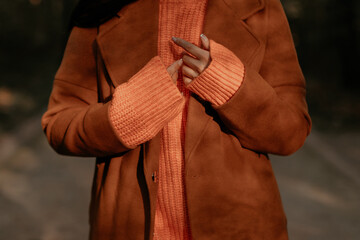 Fall clothes fashion details of knitted orange sweater and brown coat on a female figure, warm...