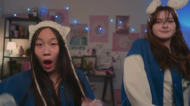 Multi-ethnic teenage girls in blue and white bomber jackets dancing to k-pop music and lip syncing for camera at home