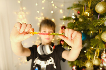 Joyful child, boy aged 10-12 with gelatin worm sweet, celebrate Christmas by playing and laughing...
