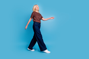 Photo of adorable lovely woman pensioner wear brown clothes go empty space isolated on blue color background