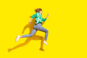 Full length photo of adorable lovely girl wear tie dye sweatshirt jumping high running empty space isolated yellow color background