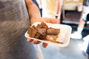 Hand holding a small styrofoam plate of wagyu beef tasting sample at Tsukiji Outer Market, Tokyo, Japan