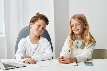 Obraz premium Boy and girl happily studying together at home, using laptops and headphones for online education The siblings are sitting at a table in their cozy living room, immersed in their elearning lessons