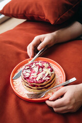 Pancakes with raspberry jam and almond flakes on a plate in male hands.