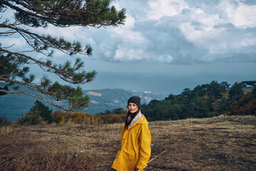 A woman in a bright yellow raincoat admiring the breathtaking scenery of mountains and trees on a peaceful hill