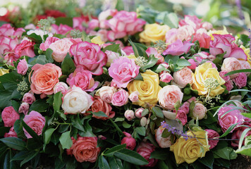 a funeral wreath of orange, pink, yellow and white roses and a white ribbon lies on a fresh grave in a cemetery
