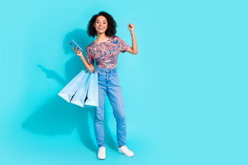 Full body photo of pretty young girl hold device shopping bags winning wear trendy colorful clothes isolated on aquamarine color background