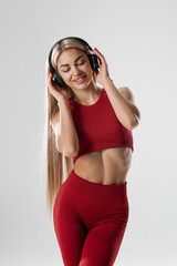 Young caucasian woman wearing headphones dancing active isolated on gray wall listening to music laughing cheerful
