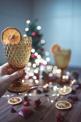 Hand holding golden wine glass with dried orange slices and christmas decoration on background