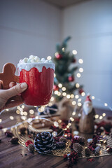 Hand holding a cup of hot chocolate with marshmallows and Christmas decoration